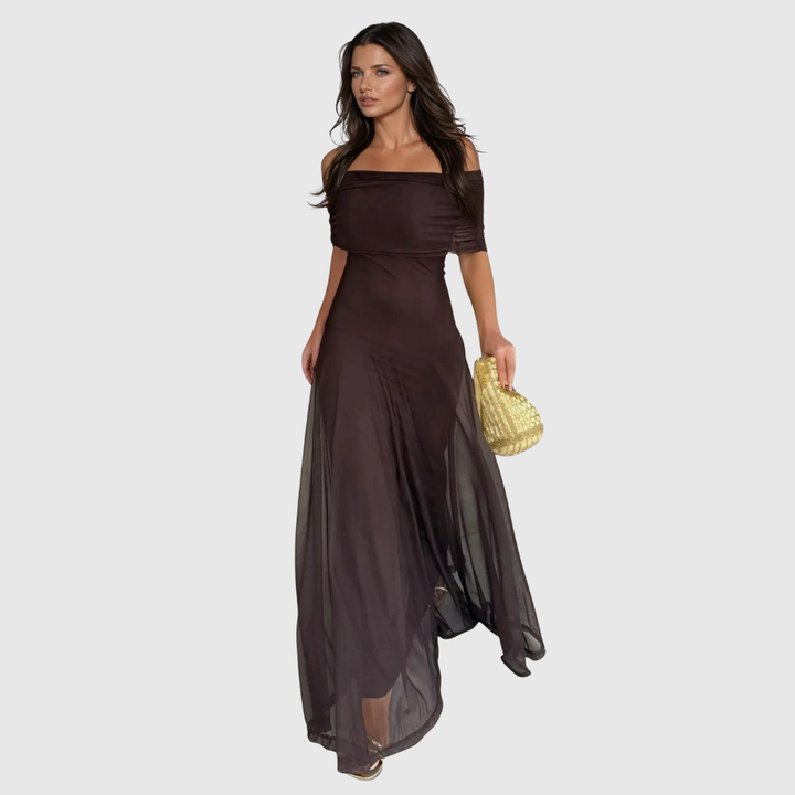 Donna che indossa un maxi abito marrone con spalle scoperte e tiene in mano una borsa intrecciata dorata