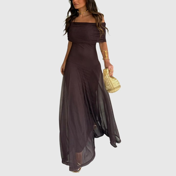 Profilo laterale di una donna con un maxi abito marrone fluido e accessori dorati