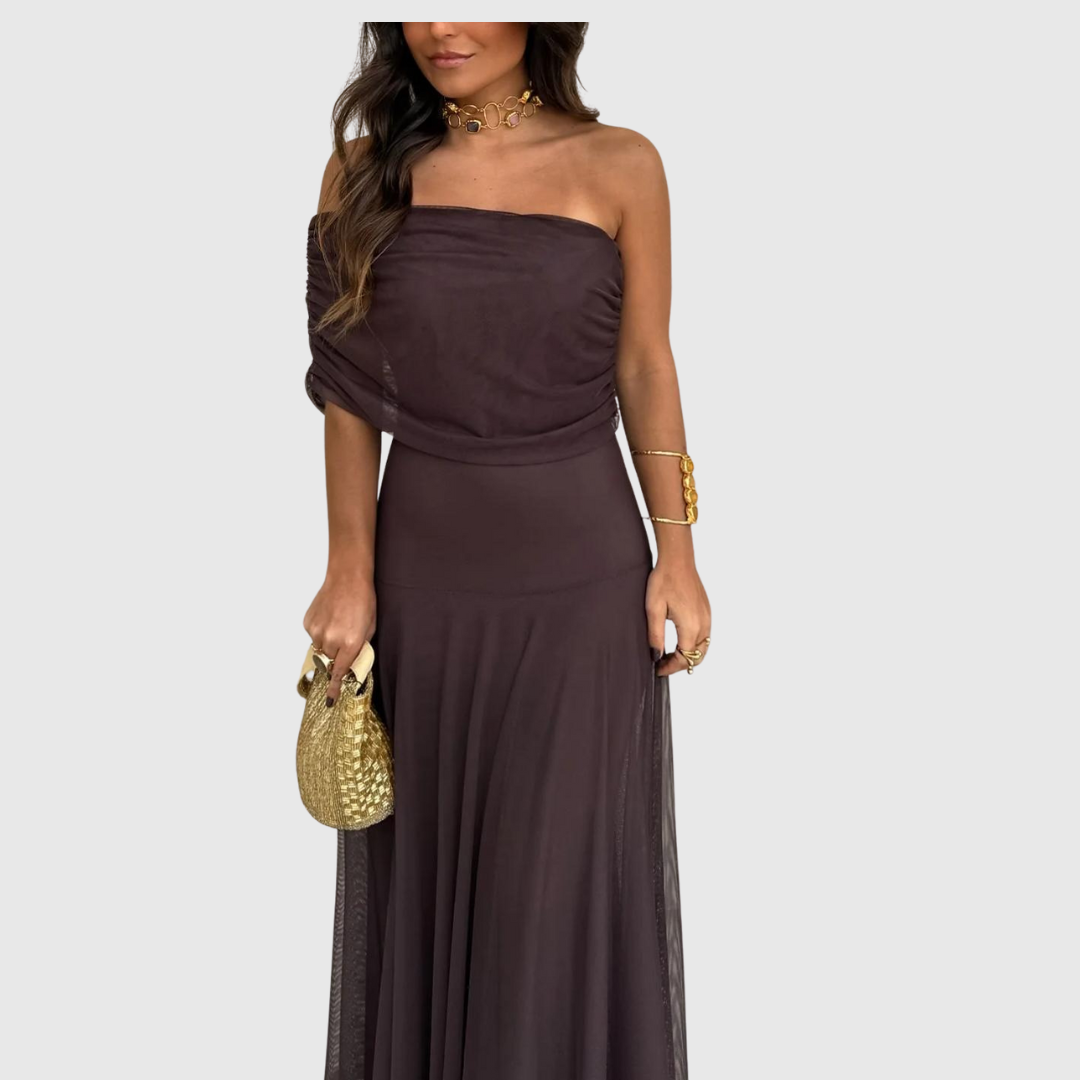 Primo piano di una donna con abito marrone con spalle scoperte, accessori dorati e borsa.