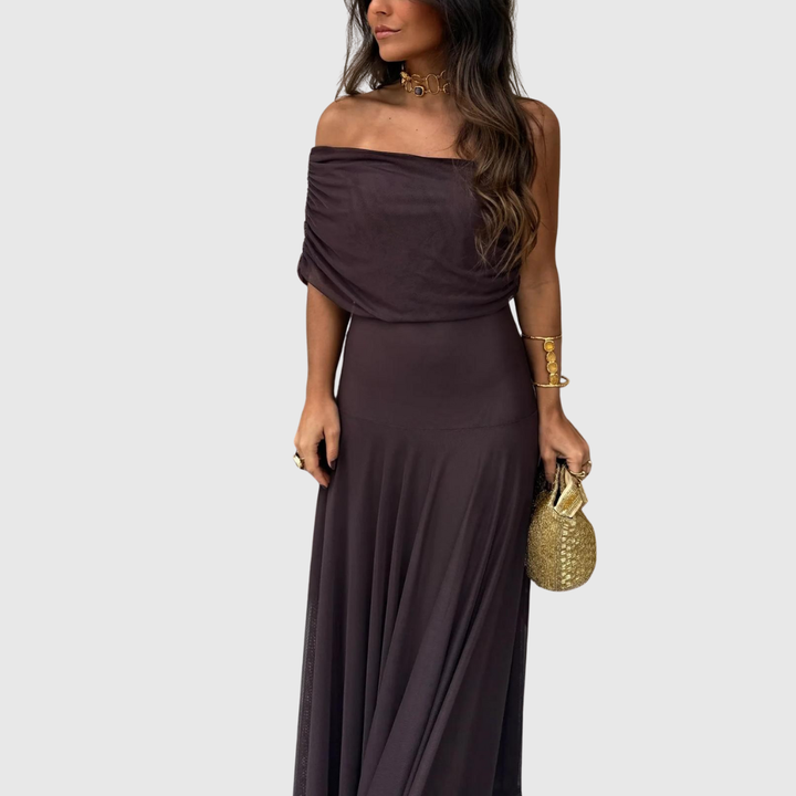 Donna con abito marrone con spalle scoperte, gioielli dorati e borsetta.